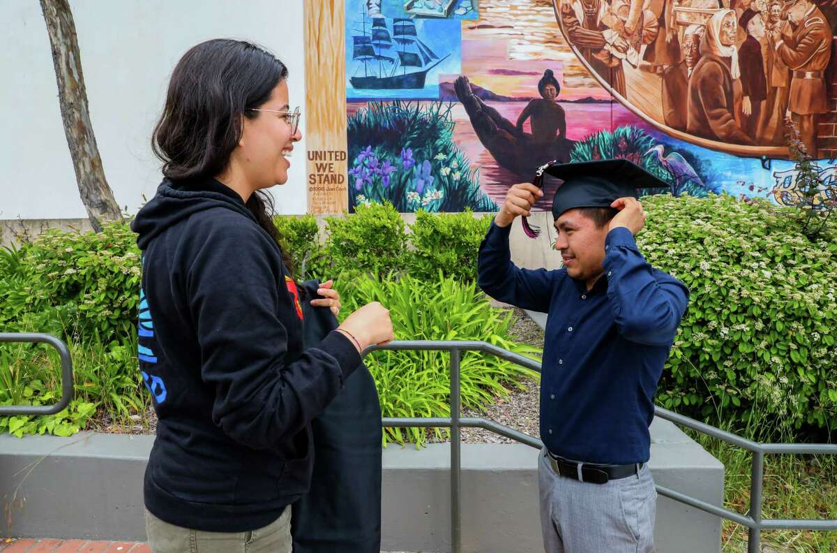 Oliser Aguilar, 21 (right), a graduate of Thurgood Marshall Academic High School, receives his cap and gown May 26 in San Francisco from school counselor Daniela Funes.  