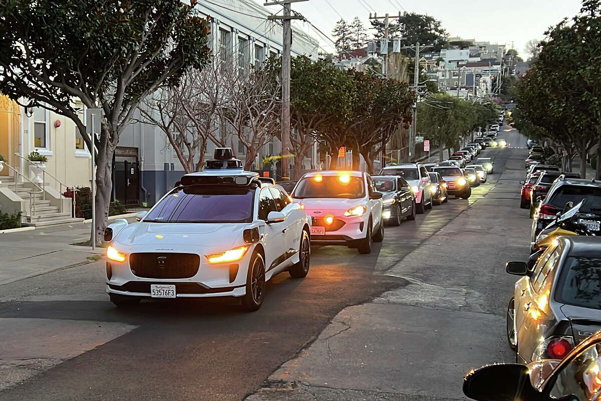 A Waymo driverless taxi stops on a street in San Francisco for several minutes because the back door was not completely shut, while traffic backs up behind it, on Feb. 15, 2023.
