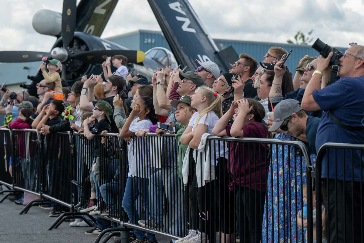 Spectators watch members of the Airborne Demonstration Team, wearing authentic gear identical to paratroopers on D-Day in 1944, jump out of a C-47 that flew on D-Day during an exhibition at the third annual Wings & Wheels showcase to benefit the Prescott Foundation, which restores and maintains WWII aircraft and vehicles, at the Hangar at 743, on Saturday in Colonie.