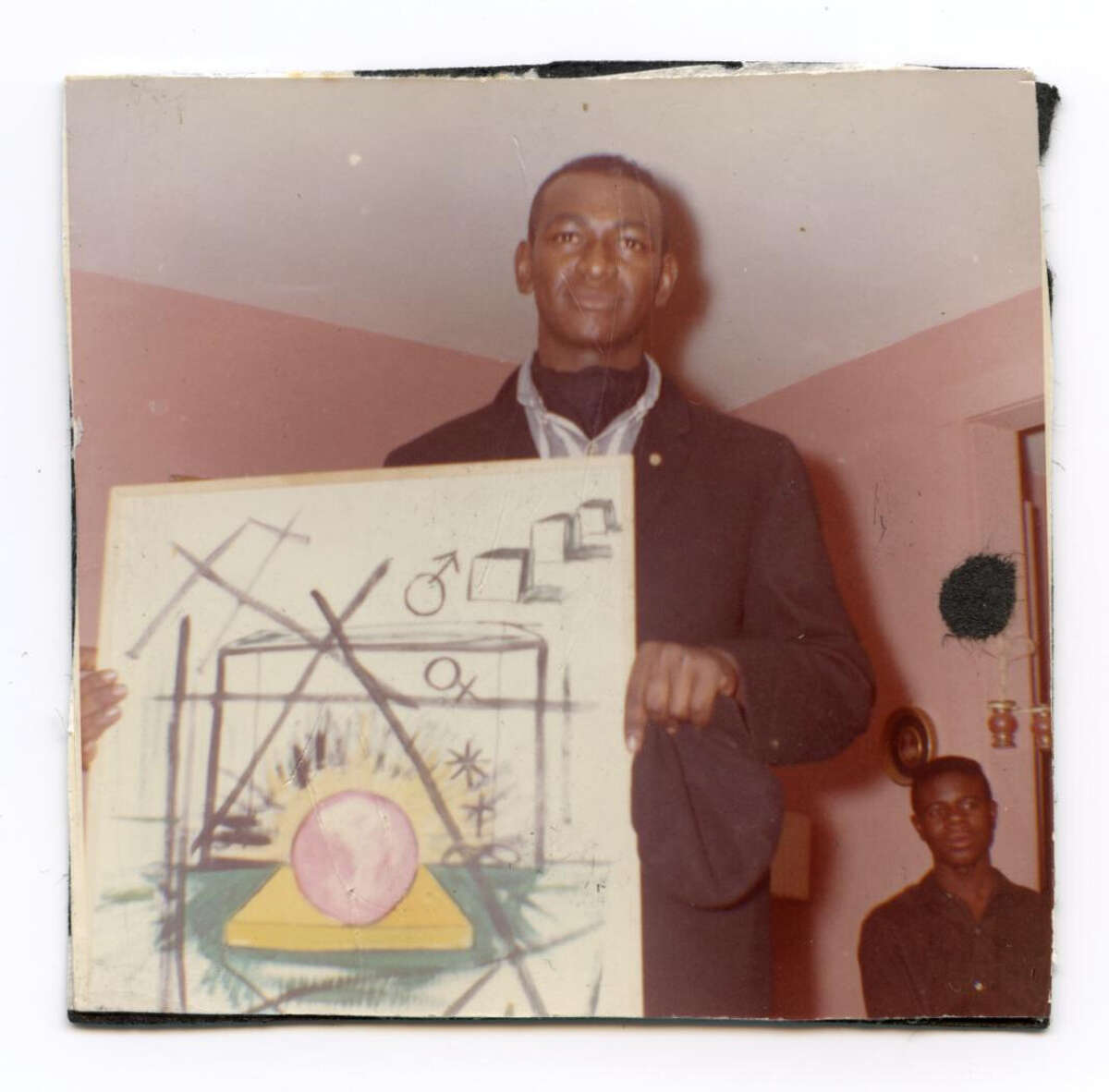 Mike Henderson with an early painting, at the home of Sandy Smith in Marshall, Mo. Smith provided a space for Henderson to hang his work; she also owned blues records that Henderson listened to. “This was when I was first turning out to be a surrealist painter,” Henderson says.