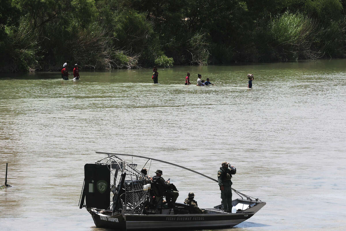 Migrants cross the Rio Grande as state troopers guard workers installing buoys on the Rio Grande south of Eagle Pass, Texas, Monday, July 10, 2023.
