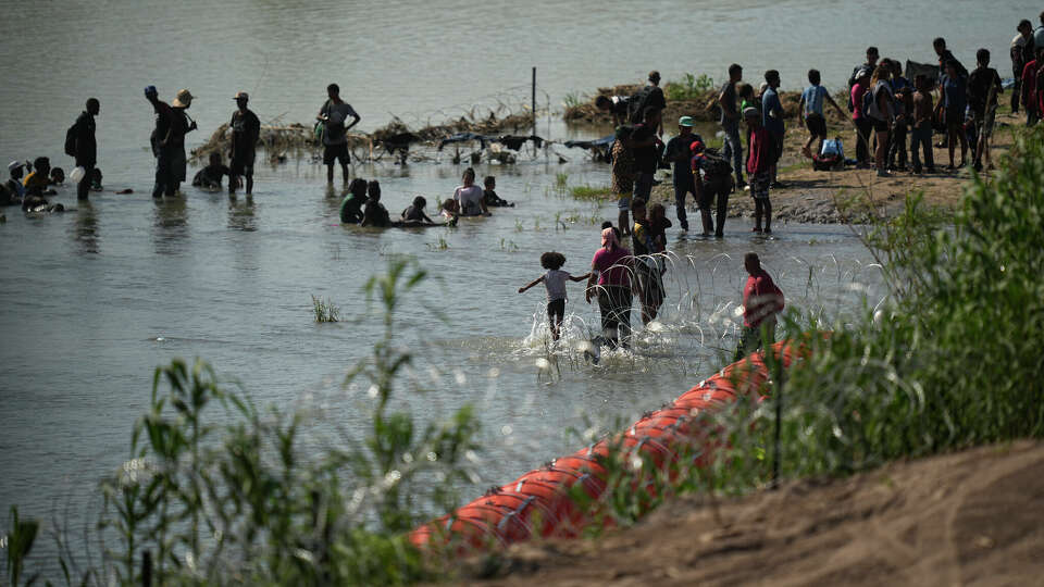 Migrants cool themselves in the waters of the Rio Grande after crossing to the U.S. from Mexico near a site where the state is installing large buoys to be used as a border barrier along the Rio Grande near Eagle Pass, Texas, Monday, July 10, 2023. (AP Photo/Eric Gay)