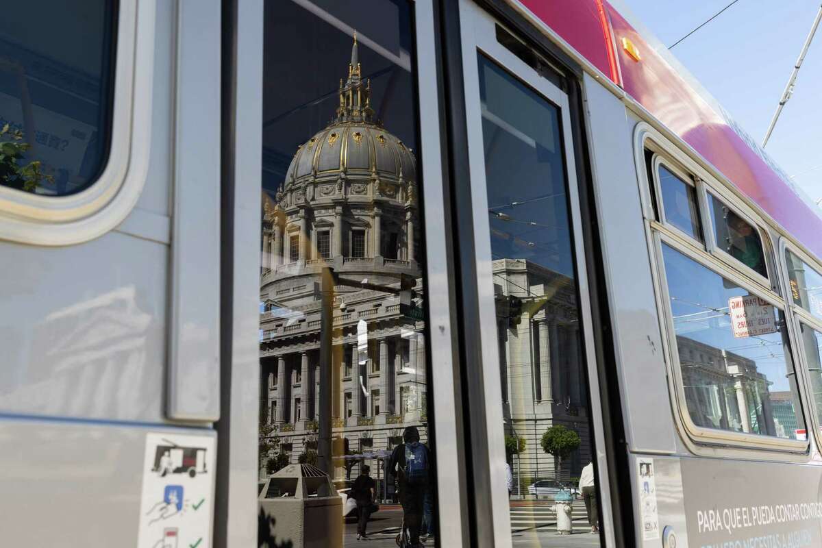 City Hall reflects from a bus window on McAllister Street in San Francisco on Thursday.