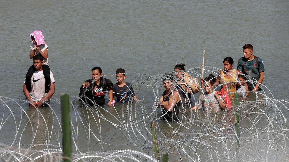 Migrants look for a way through the concertina wire on the banks of the Rio Grande south of Eagle Pass, Texas, Tuesday, July 11, 2023.