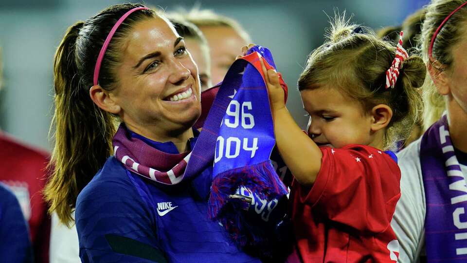 FILE -United States' Alex Morgan holds her daughter, Charlie, as she listens to Cindy Parlow Cone, president of the U.S. Soccer Federation, speak during an event with the federation, U.S. Women's National Team Players Association and the U.S. National Soccer Team Players Association at Audi Field in Washington, Tuesday, Sept. 6, 2022. Morgan says she feels calmer heading into this World Cup and wants to represent mom athletes. She's one of three mothers on this U.S. squad and is often accompanied by 3-year-old daughter Charlie. (AP Photo/Julio Cortez, File)