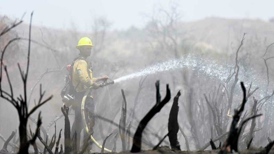 A firefighter sprays down the remaining hot spots on Monday, July 17, 2023, west of Perris, due to the Gavilan Hills bush fire that erupted on Saturday near Lake Mathews. (Anjali Sharif-Paul/The Orange County Register via AP)