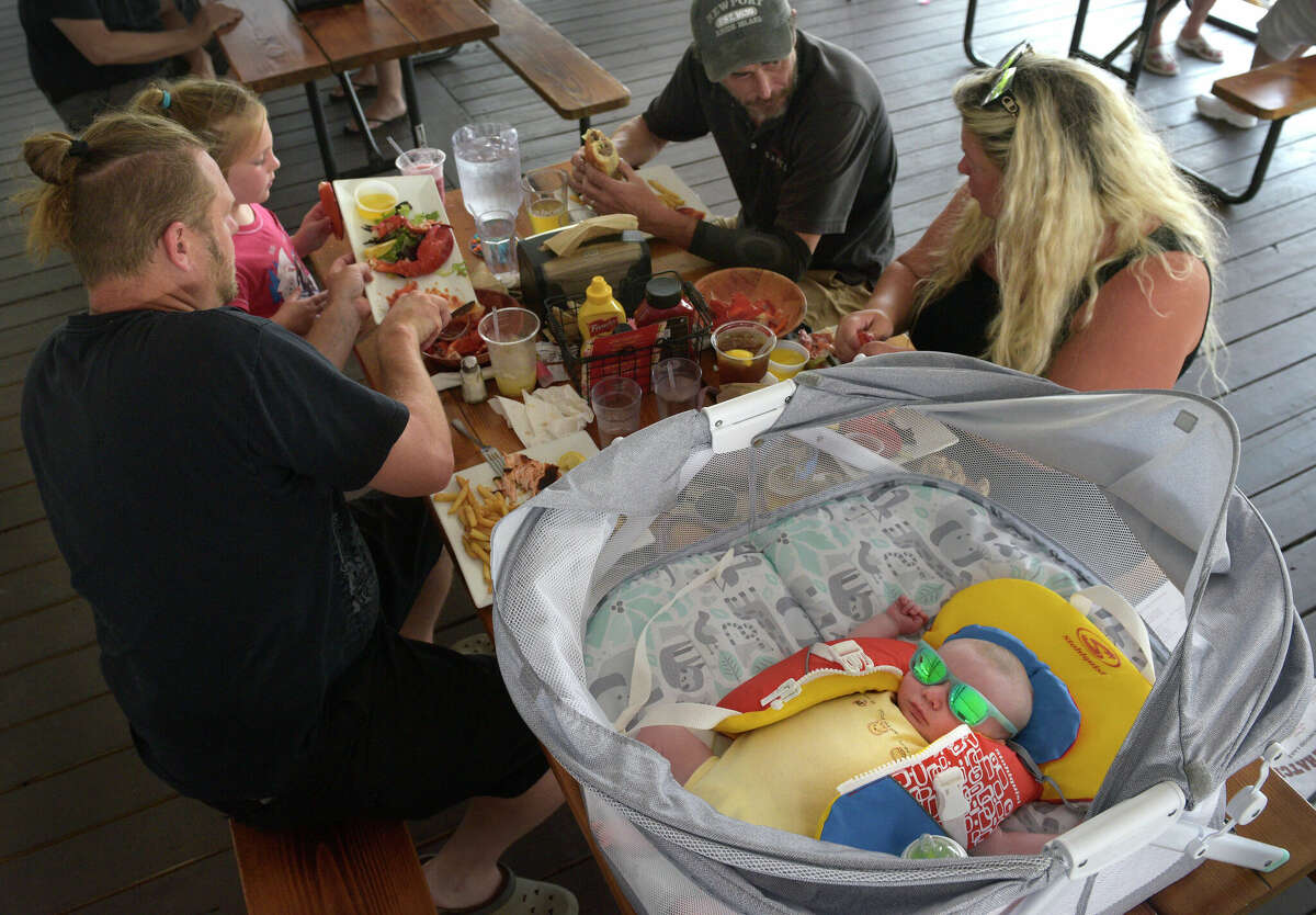 Gavin Michelson, 2-month-old, of New Fairfield, sleeps while his family, mom Annie, dad Matt, sister Aria and family friend Paul, eat lunch at the Down the Hatch restaurant on Candlewood Lake Road.  The restaurant has a dock that can be pulled up to boaters.  Candle Lake has had a positive impact on the local economy and its role in attracting more people to local restaurants and businesses.  Thursday, July 20, 2023, Brookfield, Conn.