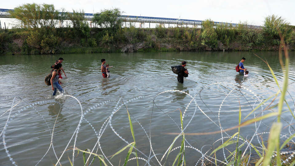 Migrants attempt to circumvent a concertina wire barrier lining the Rio Grande by walking up a creek feeding the river in Eagle Pass, Texas, Thursday, July 20, 2023.