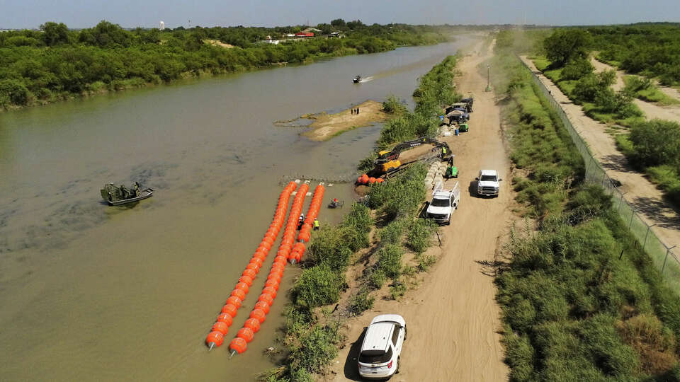 A work crew pieces together a string of buoys to be deployed on the Rio Grande south of Laredo on Tuesday, July 11, 2023. The air boats belong to the Texas Department of Public Safety. Migrants can be seen on the island.