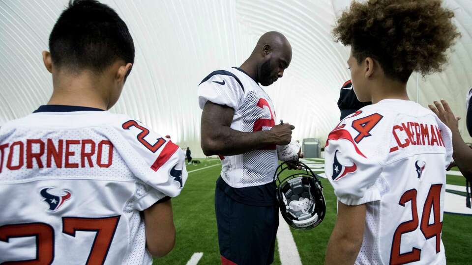 Houston Texans cornerback Johnathan Joseph, center, signs autographs for a group of youth football players at the end of practice during training camp at the Houston Methodist Training Center on Monday, Aug. 12, 2019, in Houston. The Manvel Texans football team attended practice surrounded by former Texans players where they met the players, posed for pictures and had footballs autographed.