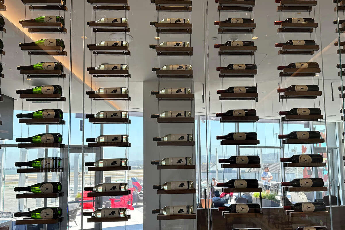 A wall of wine bottles separates the kitchen from one of the several common areas at the Maple Leaf Lounge at SFO.