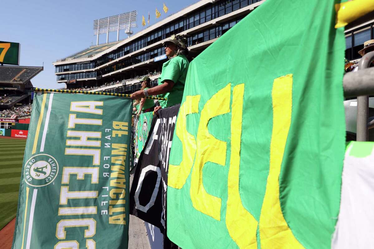 Beatriz Soria holds a flag near a “SELL” sign in the right field bleachers at the Coliseum on Saturday.