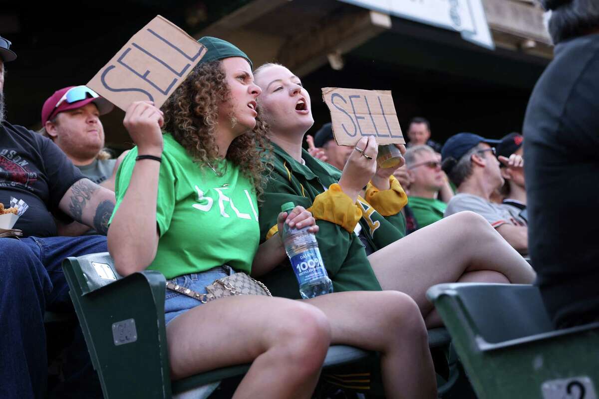Zoe Conger and Kiera Cline hold up signs in fifth inning of Saturday’s A’s-Giants game at the Coliseum with a clear message for A’s owner John Fisher: “SELL.”