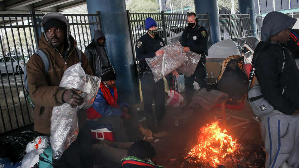 Houston Police officers Kenneth Bigger, center, and Aaron Day, center-right, hand out blankets to people as a winter storm continues to hit the area Tuesday, Feb. 16, 2021, under the elevated portion of I-45 in downtown Houston.