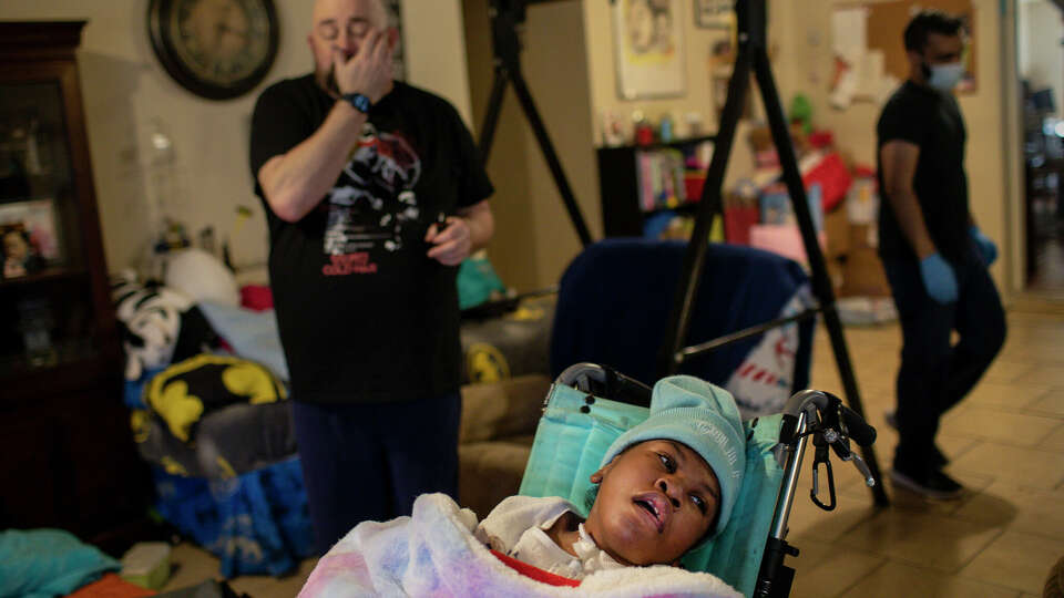 Hailey Cheevers, 11, sits in a chair in her living room as her father Stan, left, and Samir Haq, a home-health nurse, prepare the home following several days of winter storms Friday, Feb. 19, 2021, in Houston. Pipes broke in the cold weather causing parts of the ceilings to collapse.