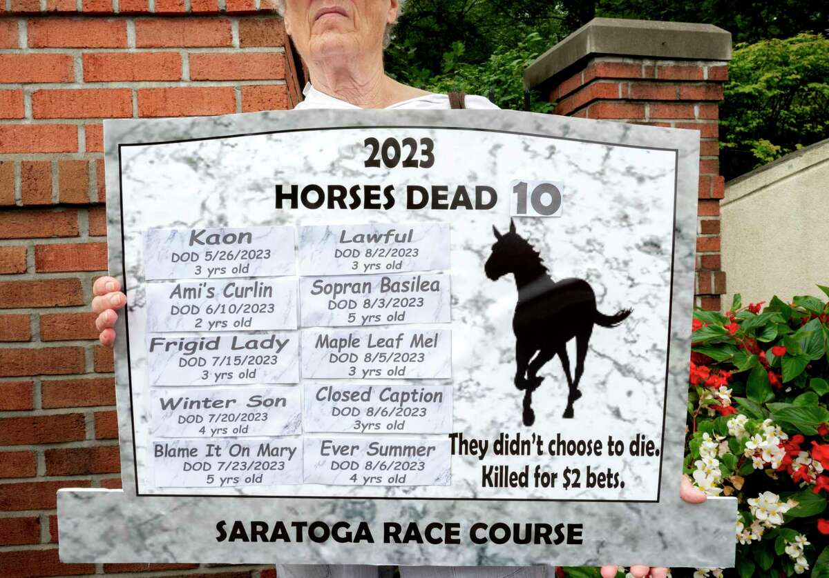 A protester holds a sign in the shape of a grave stone with the names of the horses who have died so far at Saratoga Race Track this year while standing outside the racetrack in Saratoga Springs, N.Y. on Sunday, Aug. 13, 2023. The protest was organized by the organization Horseracing Wrongs. (Lori Van Buren/Times Union)