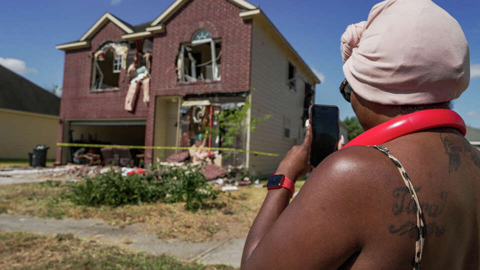 Neighborhood resident Tara McCullough, 40, shows her mother through her phone a home in the 11500 block of Silhouette Ridge in northeast Harris County which was torn apart last night after law enforcement ripped away an exterior wall of the house to create an opening, in order to get to Terran Green, 34, who barricaded himself in the home on Friday, Aug. 18, 2023, in Houston.