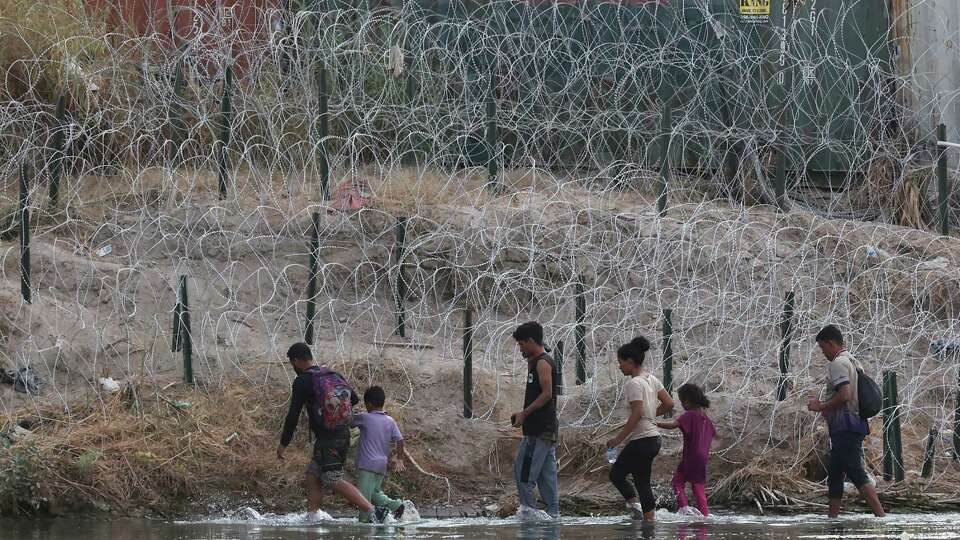 Migrants walk the Rio Grande by Shelby Park in Eagle Pass, Texas, Monday, Aug. 21, 2023. The rail cars and concertina wire are part of Gov. Greg Abbott's Operation Lone Star.