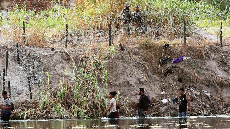 Migrants walk the Rio Grande as Texas National Guard keep guard on the banks by Shelby Park in Eagle Pass, Texas, Monday, Aug. 21, 2023.