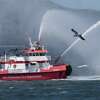 A seagull flys past a San Francisco Fire Department boat participating in a parade during Pacific Inter Yacht Association’s Opening Day on the Bay in San Francisco, Calif., on Sunday, April 30, 2023. Dozens of boats participated in the parade event despite having to battle gusty winds.