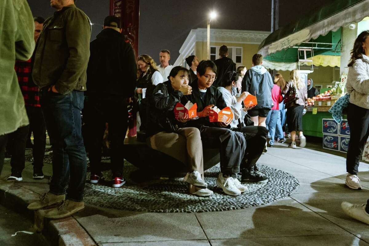 Celine and Johnny, who did not want to give their last name, eat on a bench at the Night Market in the Sunset District of San Francisco Friday.
