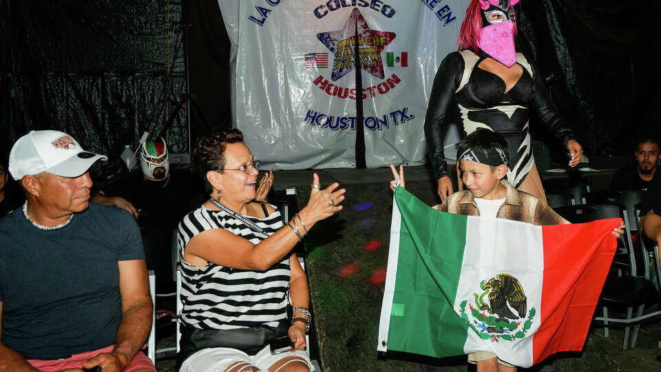 Fans hold their hands out to greet Luchadora LA Spooky and her son during a Lucha Libre fight at Coliseo Houston 