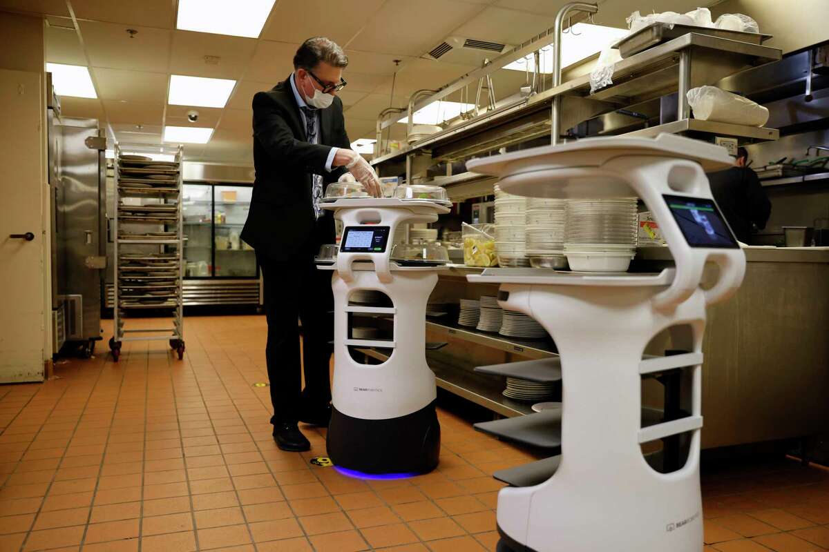 Jamie Gerkowski places hot meals on a delivery robot at the San Francisco Towers retirement community in February. New technology is raising questions about automation and labor.