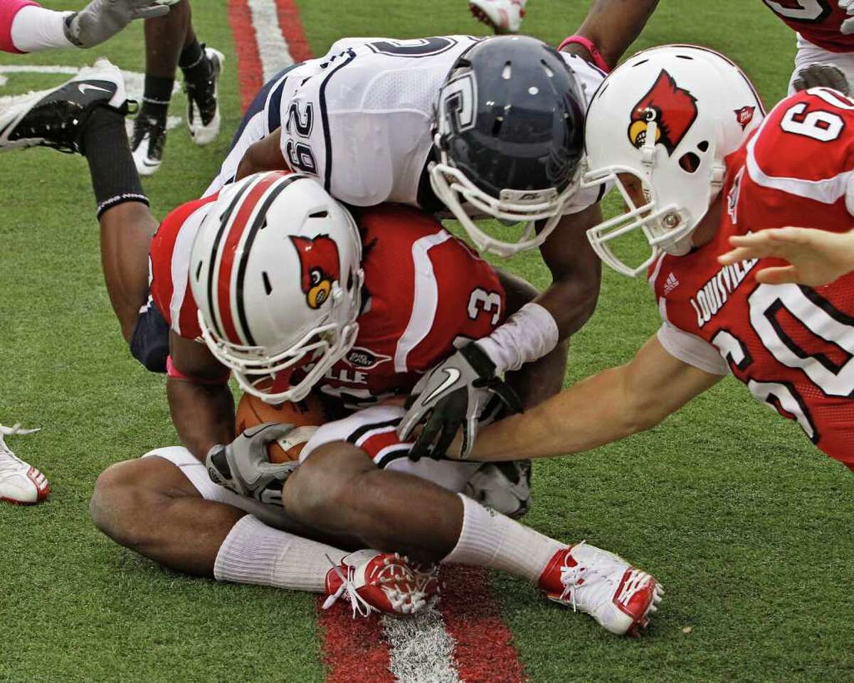 Louisville's Deon Rogers (43) covers the ball after Connecticut's Taylor Mack (29) fumbled a punt during first half action in their NCAA college football game at Cardinal Stadium in Louisville, Ky., Saturday, Oct. 23, 2010. At right is Louisville's Daniel Weedman (60). The fumble led to a touchdown. (AP Photo/Garry Jones)