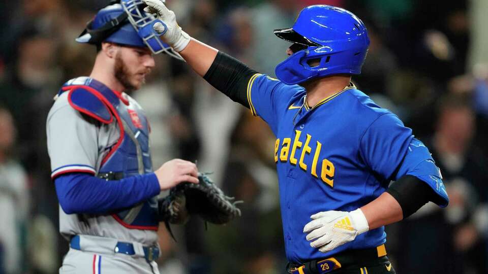 Texas Rangers catcher Jonah Heim, left, looks down as Seattle Mariners' Ty France, right, waves while crossing home plate after hitting a solo home run during the third inning of a baseball game Friday, Sept. 29, 2023, in Seattle. (AP Photo/Lindsey Wasson)