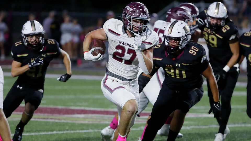 Magnolia running back Hunter Andrews (27) makes a gain in the hole between Magnolia West defenders Case Luckman (21) and Johnathan Solis (90) during the first half of their District 10-5A high school football game held at Mustang Stadium Friday, Oct. 6, 2023 in Magnolia, TX.