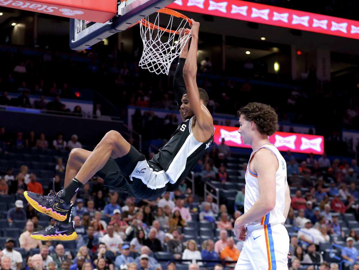 San Antonio Spurs center Victor Wembanyama, left, dunks next to Oklahoma City Thunder guard Josh Giddey, right, in the first half of a preseason NBA basketball game Monday, Oct. 9, 2023, in Oklahoma City. (AP Photo/Sarah Phipps)