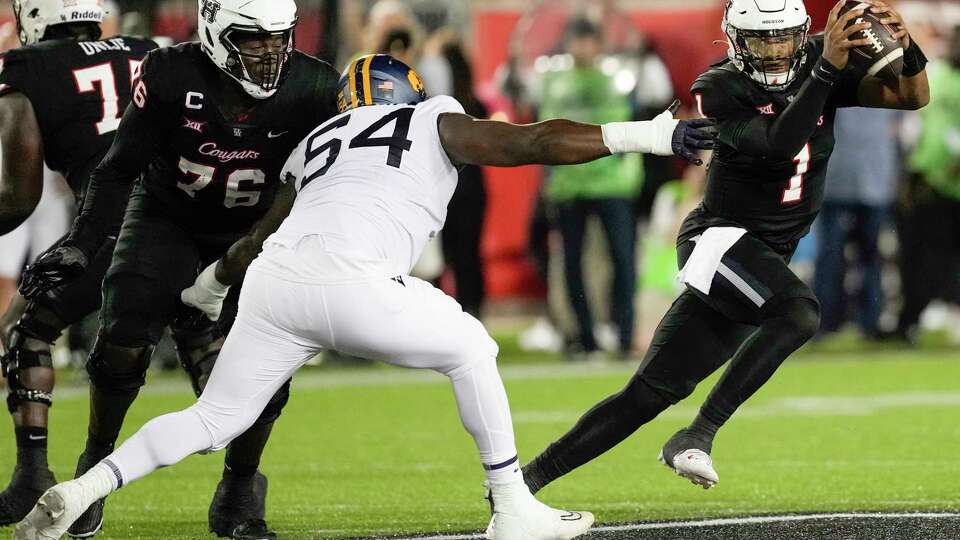 Houston quarterback Donovan Smith (1) avoids the rush from West Virginia defensive lineman Fatorma Mulbah (54) during the second half of an NCAA college football game Thursday, Oct. 12, 2023, in Houston.