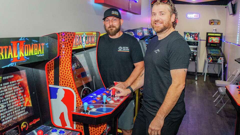 Owners Justin Ellis and Nik Green stand near the NBA Jam arcade game, the game that Ellis credits as inspiration for his arcade concept, and one of a variety of modern and retro style arcade and pinball machines available to play inside the custom built structure at 80 Retro Arcade, Tuesday, Oct. 17, 2023 in Willis.