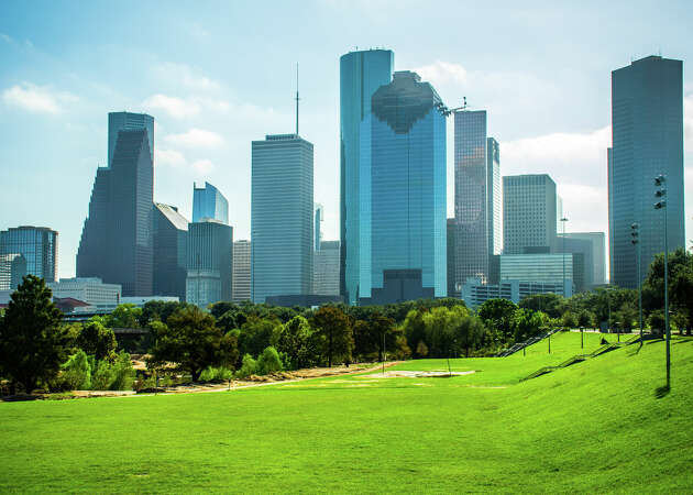 Green grass park at Buffalo Bayou River Park with Houston skyline background sunny day on a nice sunny day in the big city of Texas. Tall towers and cityscape view from the public park