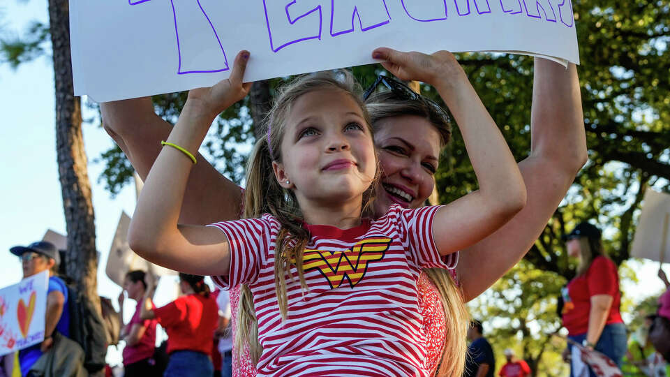 Michelle Colvard and her daughter Anja Colvard, 7, hold up signs as they join parents, teachers, students and community members and The Houston Federation of Teachers in protesting the current state of HISD schools in front of HISD headquarters on Friday, Oct. 20, 2023, in Houston.