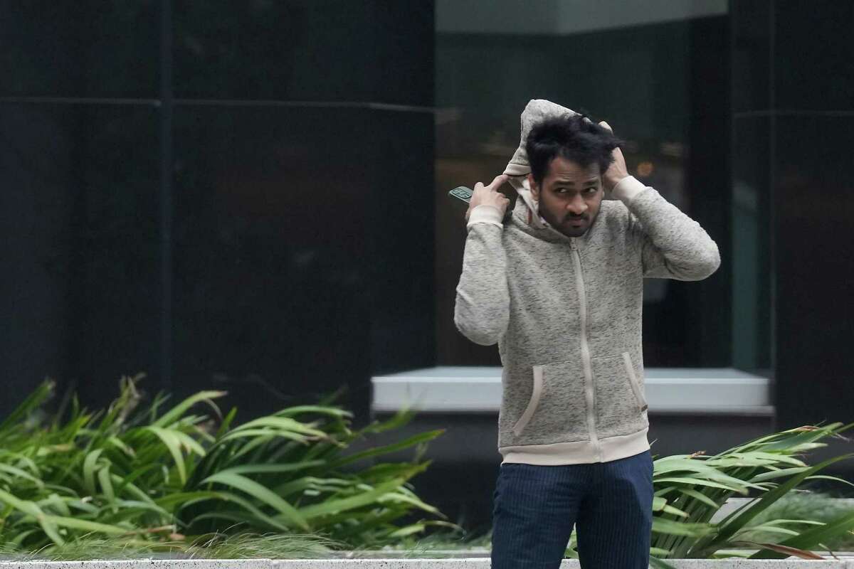 A pedestrian works on securing his hood on in the wind while walking in downtown on Monday, Oct. 30, 2023 in Houston. A strong cold front pushed Houston's temperatures lows into the 40's.