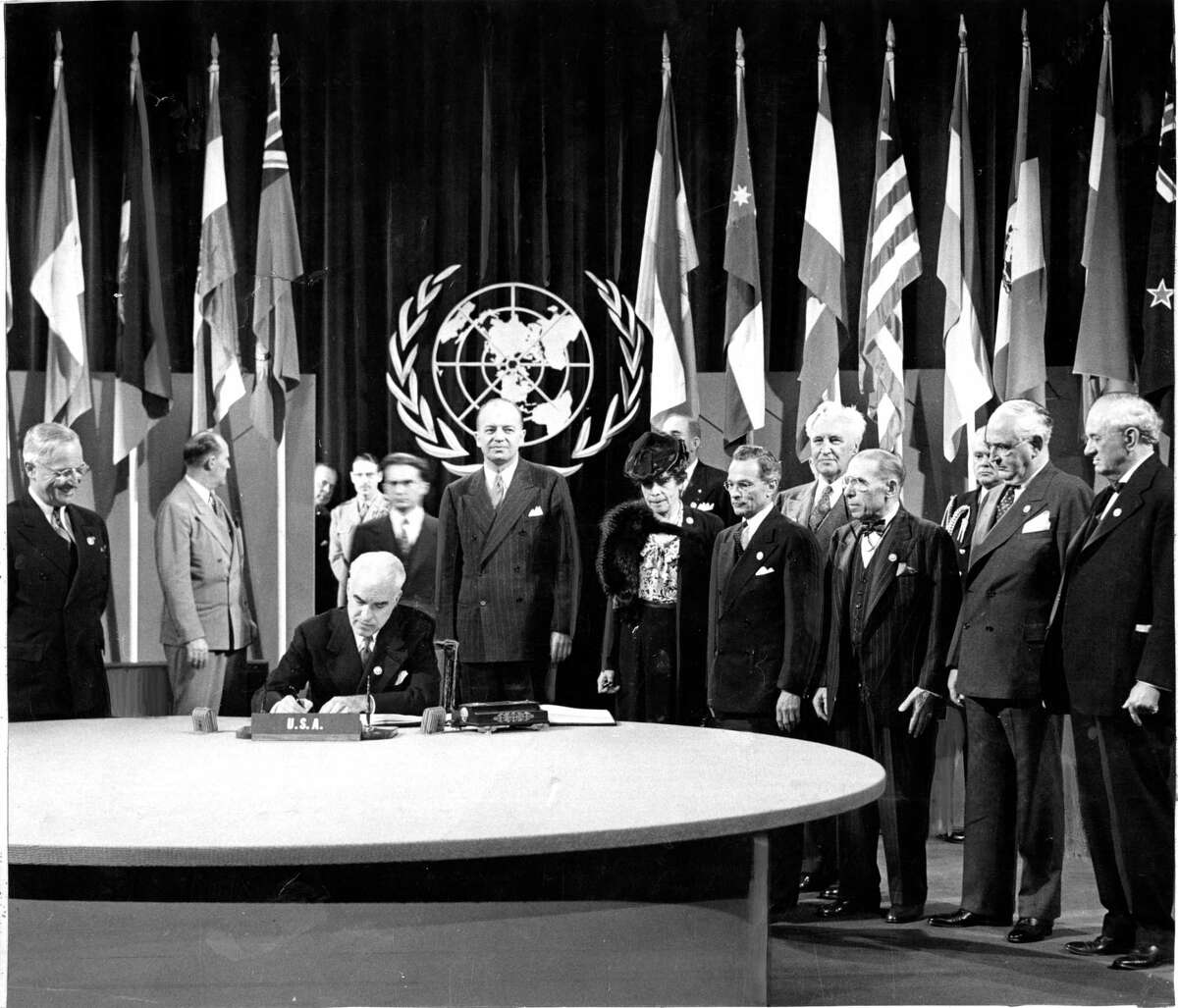 President Harry Truman watches as Secretary of State Edward Stettinius signs the U.N. Charter for the United States.