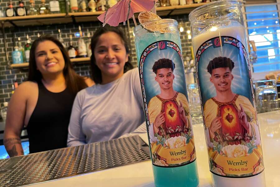 Picks Bar owners Amber Hernandez and Jessica Marinez pose with their specially designed Victor Wembanyama prayer candle, which doubles as a collins glass for cocktails. San Antonio artist Silvy Ochoa designed the candle, which is available exclusively at Picks Bar as well as the bars Pink Shark and Sore Loser.