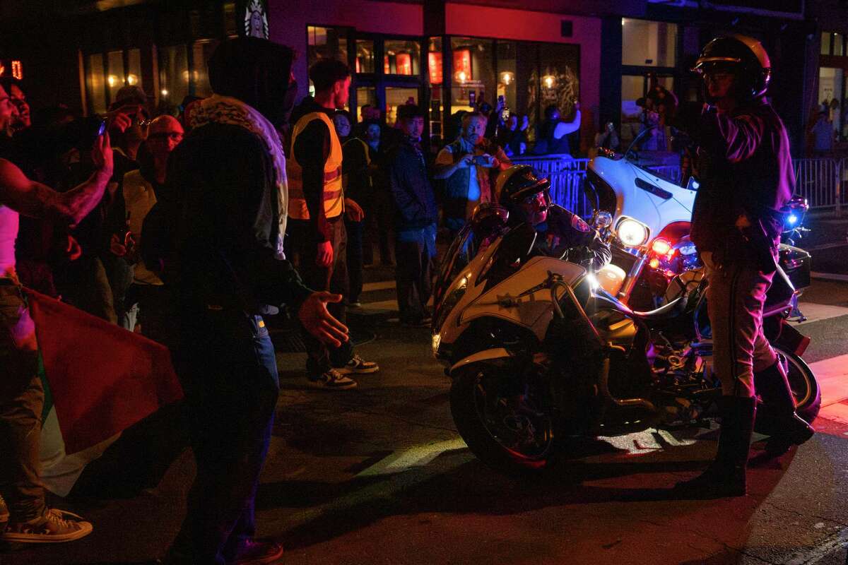 A California Highway Patrol officer takes a defensive stance while a fellow officer recovers his tipped-over motorcycle as protestors march on Kearney Street demanding a ceasefire of the ongoing Israel-Palestine conflict, during the 2023 Asia-Pacific Economic Cooperation Economic Leaders’ Week (APEC) in San Francisco, Tuesday, Nov. 14, 2023.