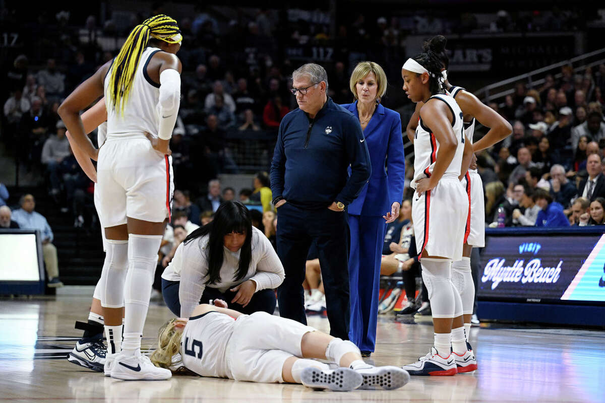 UConn coach Geno Auriemma, center, looks down at injured guard Paige Bueckers (5) during the first half of the team's NCAA college basketball game against Maryland, Thursday, Nov. 16, 2023, in Storrs, Conn. (AP Photo/Jessica Hill)