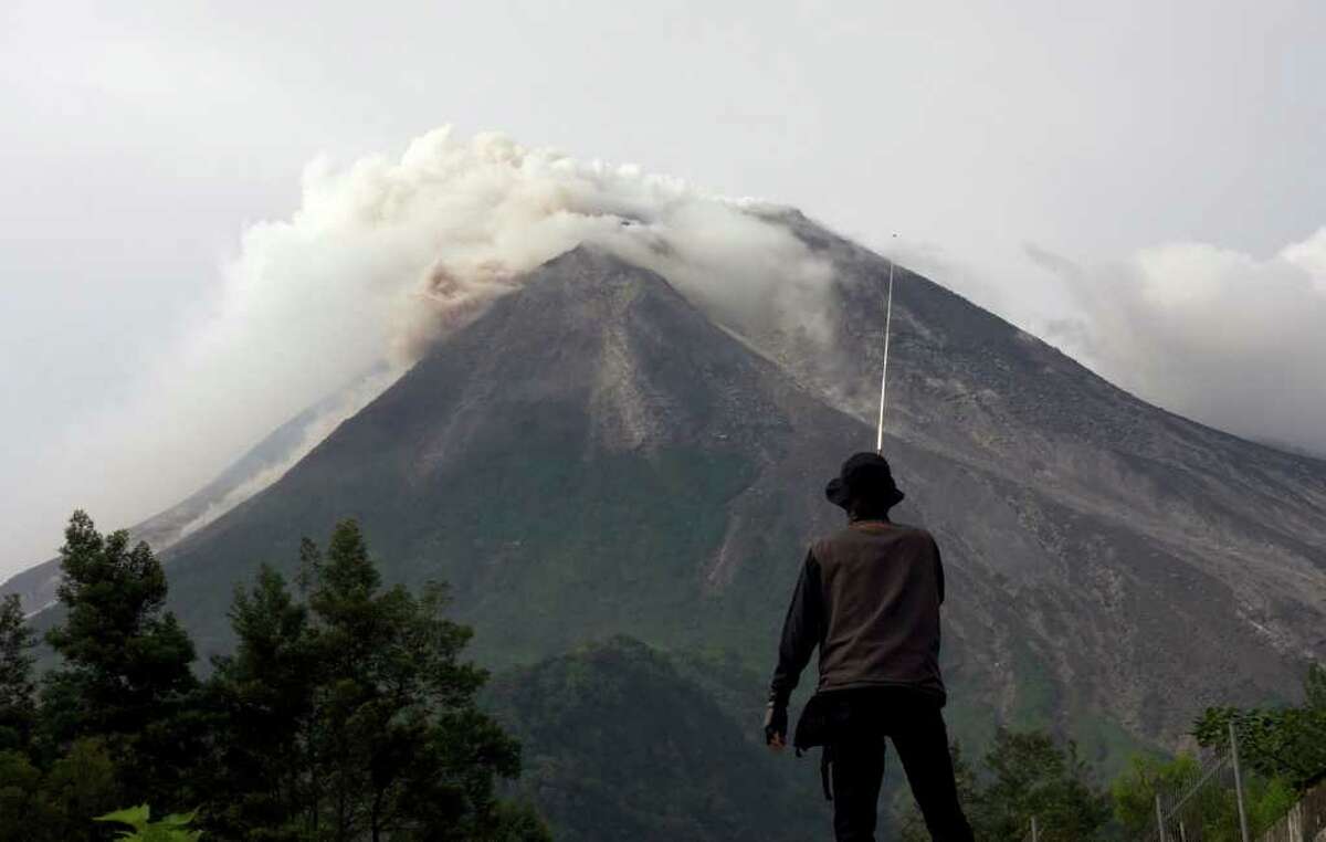 A volunteer watches as Mount Merapi spews volcanic smoke in the background in Kaliadem, Yogyakarta, Indonesia, Tuesday, Oct. 26, 2010. Indonesia's most volatile volcano started erupting Tuesday, after scientists warned that pressure building beneath its dome could trigger the most powerful eruption in years. (AP Photo/Gembong Nusantara)