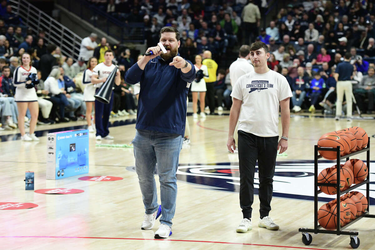 On-court host Conor Geary, left, introduces a student participating in a three-point shooting contest during UConn's men's basketball game at Gampel Pavilion in Storrs, Conn. Monday, Nov. 27, 2023.