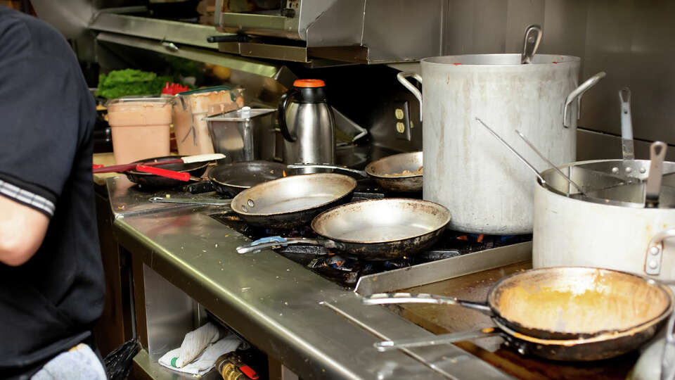 A view of a busy restaurant kitchen cooking area, featuring stockpots, grilled food and clutter.