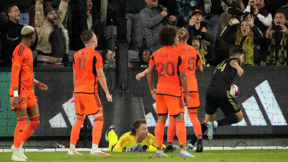 Houston Dynamo goalkeeper Steve Clark, below, looks up after a goal by Los Angeles FC midfielder Ryan Hollingshead, right, during the first half in the MLS playoff Western Conference final soccer match Saturday, Dec. 2, 2023, in Los Angeles. (AP Photo/Marcio Jose Sanchez)