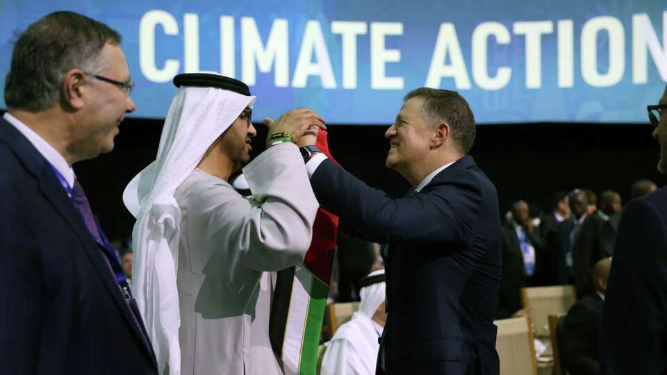 Majid Jafar, chief executive officer of Crescent Petroleum Co., right, gives Sultan Ahmed Al Jaber, chief executive officer of Abu Dhabi National Oil Co. (ADNOC) and president of COP28, center, a scarf in the colours of the United Arab Emirates national flag during the Summit on Methane and Other Non-CO2 Greenhouse Gases on day three of the COP28 climate conference at Expo City in Dubai, United Arab Emirates, on Saturday, Dec. 2, 2023. More than 70,000 politicians, diplomats, campaigners, financiers and business leaders will fly to Dubai to talk about arresting the world's slide toward environmental catastrophe. MUST CREDIT: Bloomberg photo by Hollie Adams