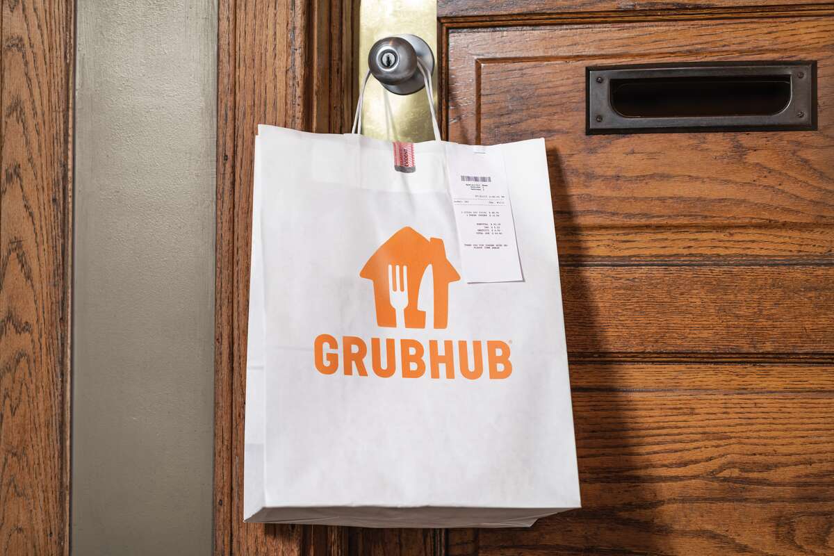 A Grubhub delivery bag hangs on a doorknob in this marketing image.