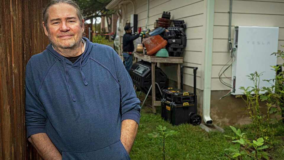 Home owner Chris Graf poses for a portrait as Adrian BallinaÕs, electrician 4 with Tesla, background, works on installing an additional energy storage unit, (battery) at his home on Thursday, November 30, 2023, in Round Rock, Texas.