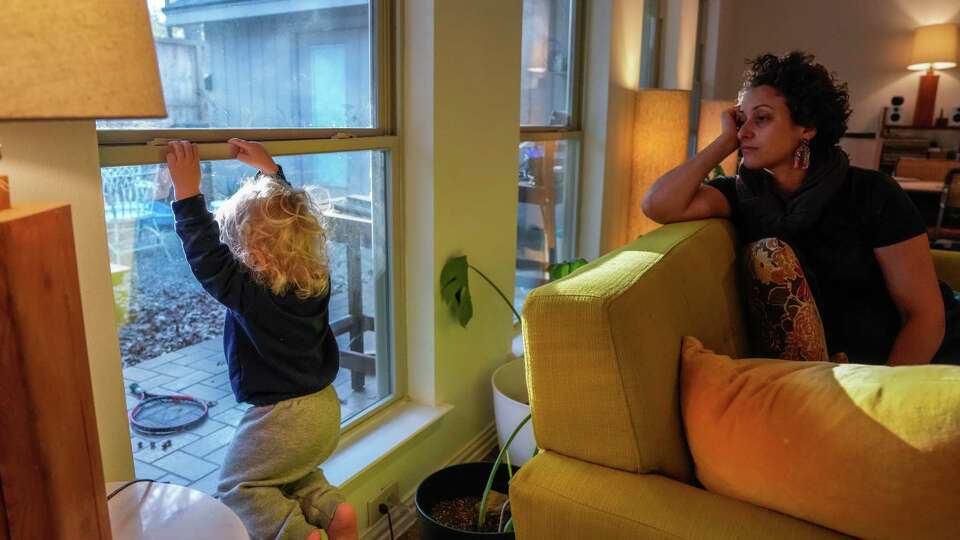 Sihem Fekih-Soibinet, 39, watches over her son Isaac Soibinet, 1, as he looks out the window of their home on Thursday, Dec. 14, 2023, in Spring. Corentin and Sihem have been juggling working remotely from home and caring for their 1 year old son after his daycare recently closed abruptly.