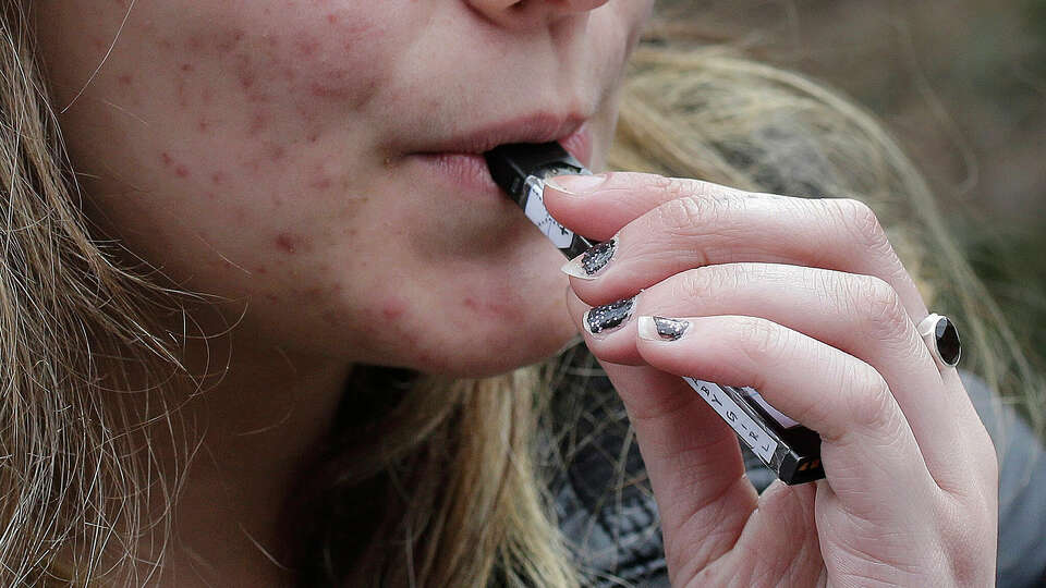  In this April 11, 2018, file photo, a high school student uses a vaping device near a school campus in Cambridge, Mass.