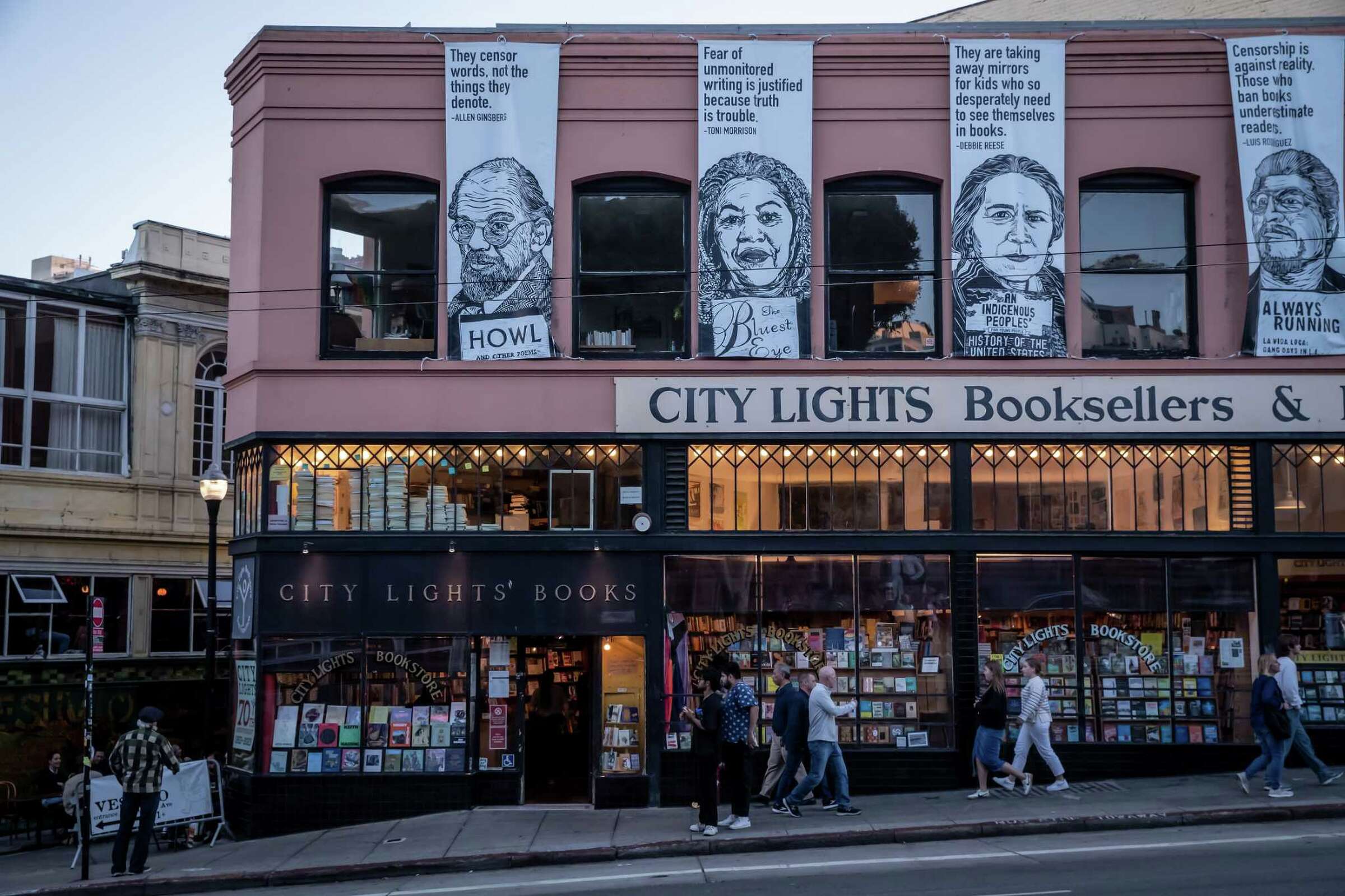 City Lights Bookstore, light brown and dark green building sparkling with dozens of lights and covered in books. The store is also covered in black and white posters of authors.